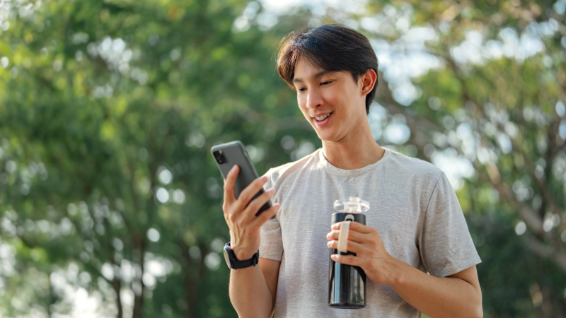 Young man looking at mobile phone while holding water bottle